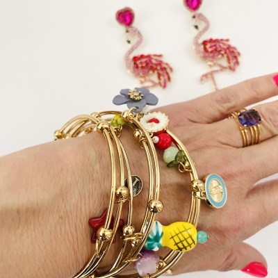 Pulseiras douradas com pingentes coloridos, anel com pedra roxa, e brincos flamingo rosa no fundo