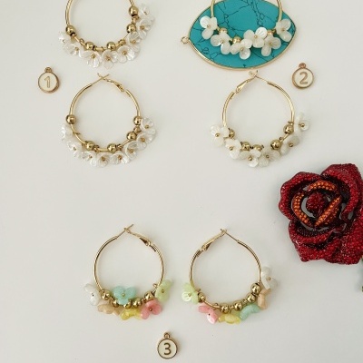 Brincos de argola dourada com detalhes florais em fundo branco com etiquetas e rosa vermelha