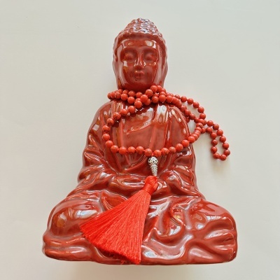 Estátua vermelha de Buda com colar de contas vermelhas e franjas sobre fundo branco