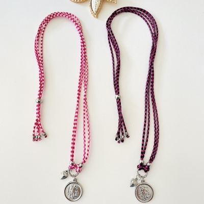 Colares rosa e roxo com pendentes prateados e broche branco com dourado no fundo branco