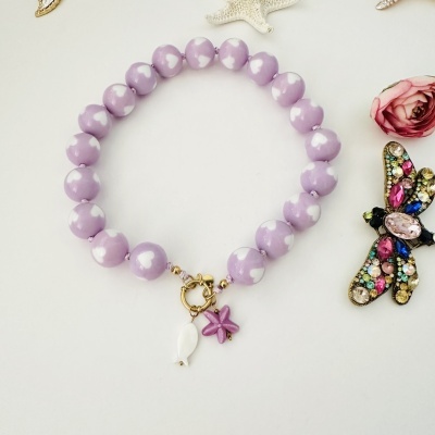 Colar com contas lilás e corações brancos com fecho dourado e pendentes, sobre fundo branco