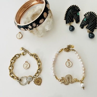 Quatro acessórios: bracelete preto com flores douradas, duas pulseiras dourada e de pérolas, e cinto fino dourado com fivela.