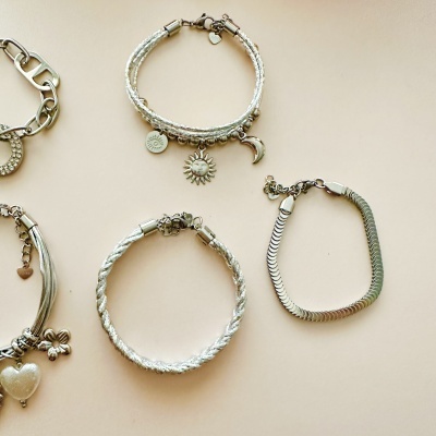 Conjunto de quatro pulseiras prateadas com diferentes estilos e pendentes sobre fundo bege.