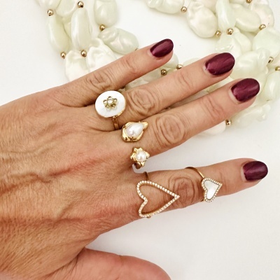 Mão com cinco anéis dourados e colar de contas brancas ao fundo