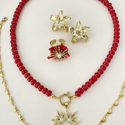 Conjunto de bijuteria com colar de contas vermelhas, pendente dourado em forma de estrela, gargantilha dourada com corações, brincos e anel dourados com pérolas e detalhes vermelhos.