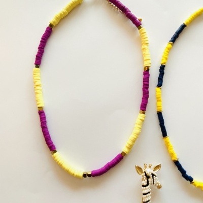 Colar de contas amarelas e roxas com fecho dourado ao lado de ornamento de girafa