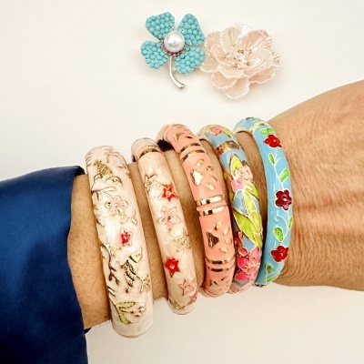 Pulseiras coloridas com padrão floral e dois broches em forma de flor sobre fundo branco