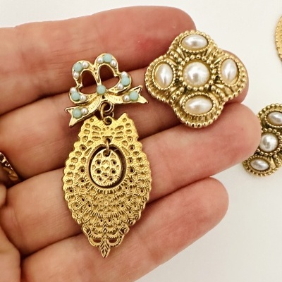 Brincos dourados com pérolas e detalhes turquesa num fundo branco