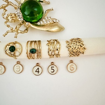 Anéis dourados com pedras verdes e broche dourado com pedra verde e cristais num fundo branco