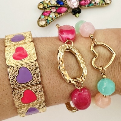 Pulseiras douradas com corações e pedras coloridas e broche em forma de insecto multicolorido
