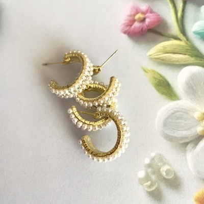 Brincos aro dourados com pérolas sobre fundo de tecido bordado com flores