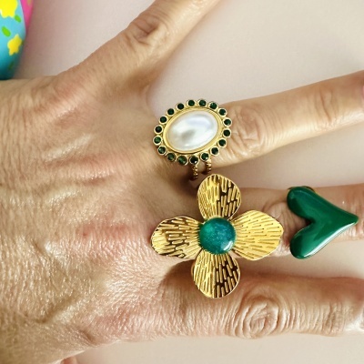 Mão com três anéis de design diferente em verde e dourado.