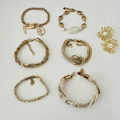 Pulseiras douradas variadas e brincos com pérolas sobre fundo branco