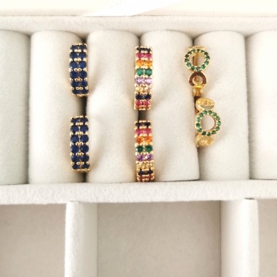 Três pares de brincos de argola em caixa de veludo branco, com pedras azuis, coloridas e verdes.