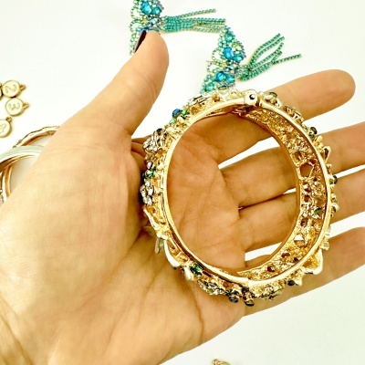 Pulseira dourada com pedras coloridas, vista em mão sobre fundo branco