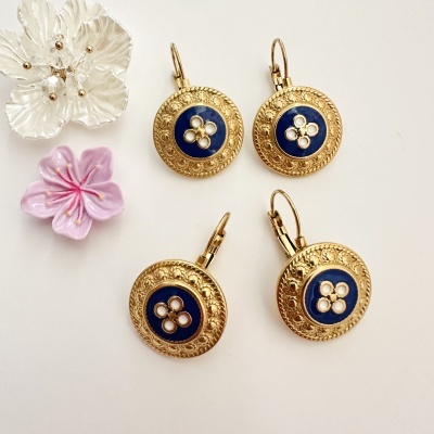 Conjunto de brincos redondos dourados com centro azul e padrão branco, acompanhado de flores decorativas
