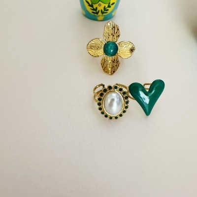 Três anéis dourados com detalhes em verde e pérola sobre fundo claro
