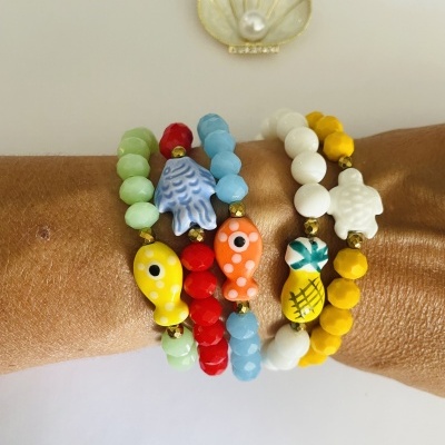 Pulseiras coloridas com contas redondas e peixes e tartarugas decorativas num braço castanho sobre fundo branco