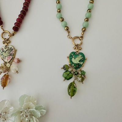 Duas pulseiras com contas coloridas e medalhões em forma de coração com imagem de ave