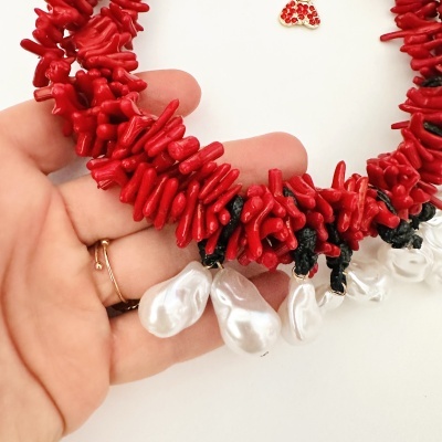 Colar de coral vermelho com pérolas brancas segurado numa mão