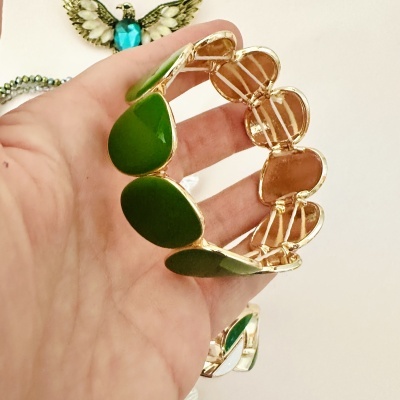 Pulseira com pedras verdes e metal dourado segurada por uma mão