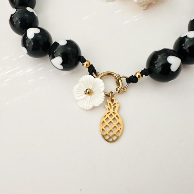 Colar com contas pretas com corações brancos e pendente dourado e flor branca