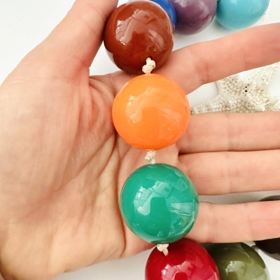 Colar de contas grandes coloridas segurado por uma mão sobre fundo branco e estrela-do-mar.