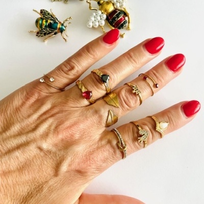 Mão com vários anéis dourados e prateados e três broches em forma de abelha em fundo branco