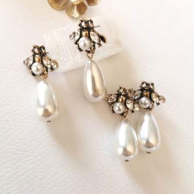 Dois pares de brincos com pérolas e cristais, um brinco com flor dourada ao fundo