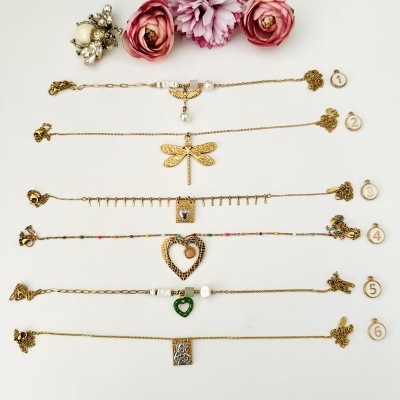 Seis pulseiras douradas com diferentes pendentes, numeradas e decoradas com flores artificiais e um broche de abelha