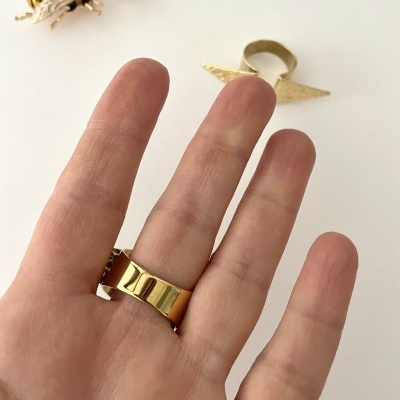 Anel dourado largo no dedo médio com brincos de abelha e anel pontiagudo dourado ao fundo