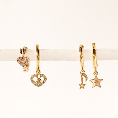 Brincos dourados com formas de coração, chave e estrela, pendurados numa barra branca