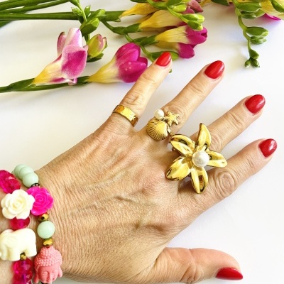 Mão com anéis dourados e pulseiras coloridas ao lado de flores mistas