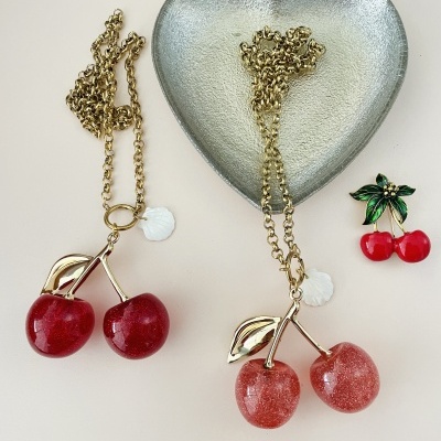 Dois colares com pendentes de cereja vermelha e rosa em corrente dourada e broche de cerejas vermelho e folhas verdes