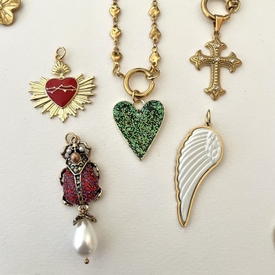Pendentes dourados coloridos com corações, cruz, asa e figura humana em fundo claro
