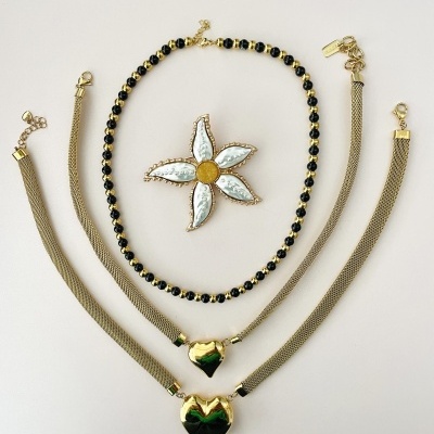 Colar com flores e pulseiras douradas com corações pretos sobre fundo branco