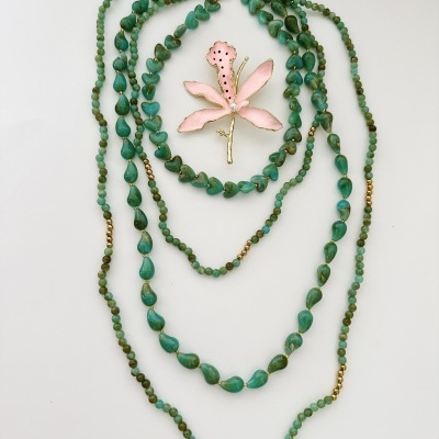 Colar verde com contas e broche floral rosa em fundo branco