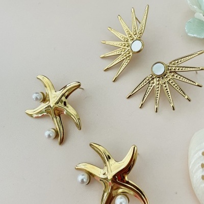 Brincos dourados com pérolas e pequenos espelhos em fundo claro