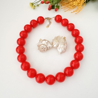 Colar vermelho com pendente de conchas brancas e flores ao fundo