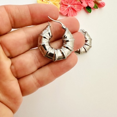 Brincos argola prateados canelados com mão segurando e flores ao fundo