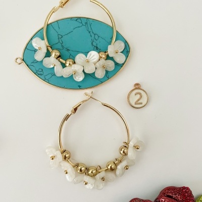 Dois brincos de argola dourados com flores brancas, um oval azul mármore, medalhão com número 2, peça decorativa vermelha brilhante