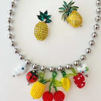 Colar com pendentes de frutas coloridas e brincos de abacaxi sobre fundo branco