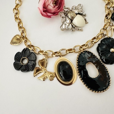Colar dourado com vários pendentes pretos e dourados junto a flor rosa