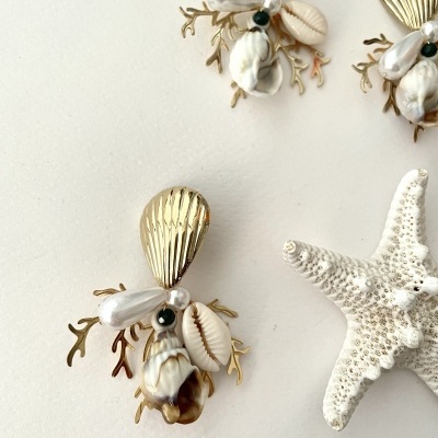 Brincos com conchas, pérola, esfera preta e elementos dourados junto de uma estrela-do-mar branca