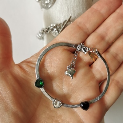 Pulseira fina prateada com corações coloridos em mão.