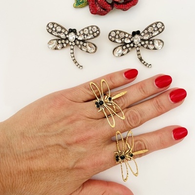 Anel e brincos em forma de libélula com cristais e metal dourado em fundo branco com flor vermelha.