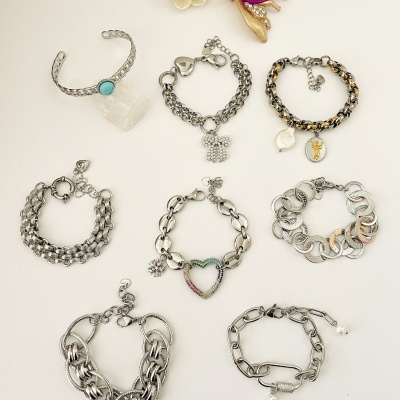 Pulseiras metálicas e broche dourado com pedra roxa e flor branca sobre fundo branco