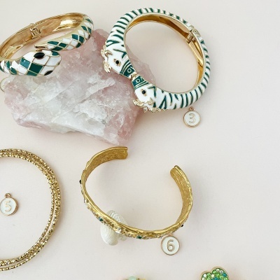 Braceletes dourados com padrões verde e branco sobre pedra rosa