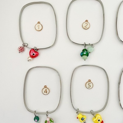 Pulseiras finas quadradas com pendentes de vidro coloridos e números em círculo de madeira.