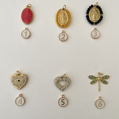 Seis pingentes variados com números em etiquetas pequenas, incluindo imagens religiosas e formas de coração e libélula.